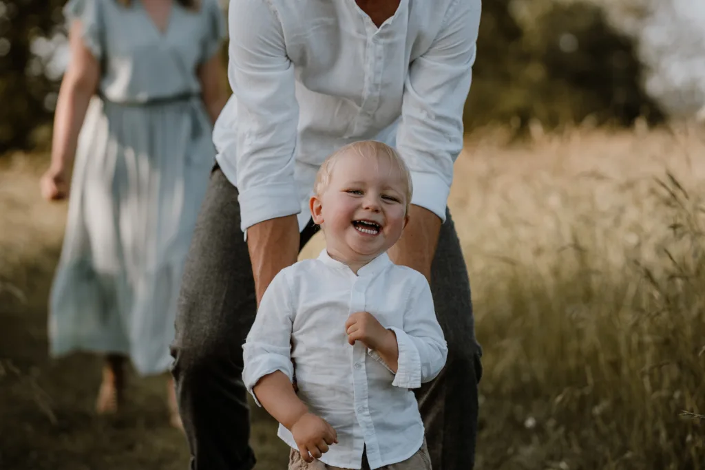 Vater hilft seinem kleinen Sohn beim Laufen auf einem Wiesenweg