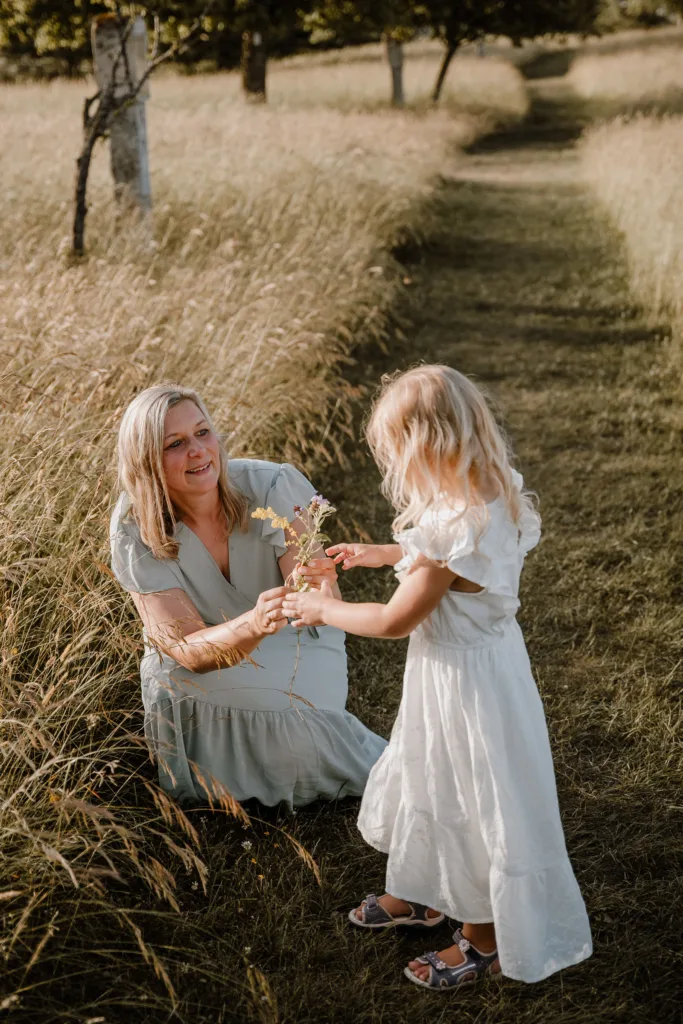 Mutter kniet auf einer Wiese und bekommt von ihrer Tochter Blumen geschenkt