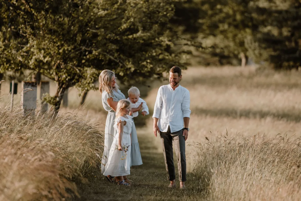Familie mit zwei Kindern läuft gemeinsam über einen Wiesenweg im warmen Abendlicht.
