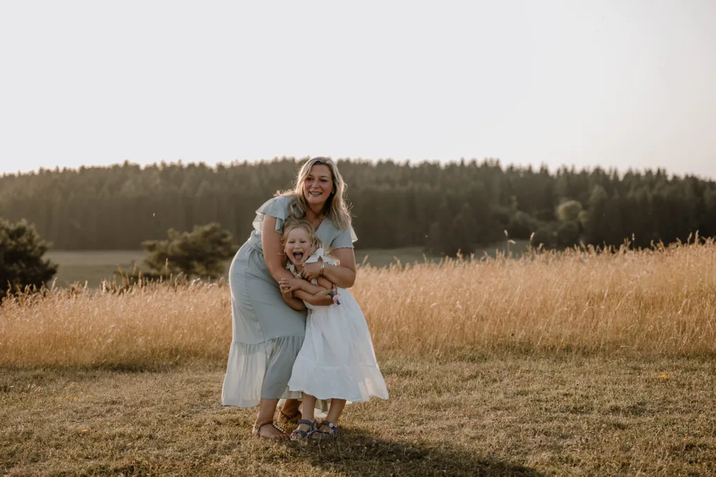 Mutter umarmt lachende Tochter auf einer Wiese im goldenen Abendlicht.