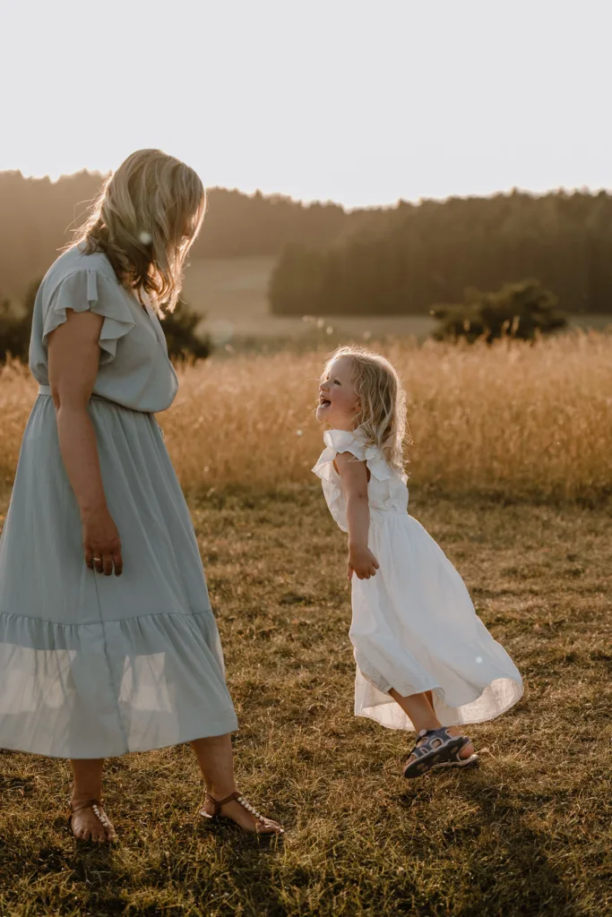 Mama und Tochter lachen sich bei einem natürlichen Familienshooting in der Abendsonne auf einer Wiese bei Rottweil an