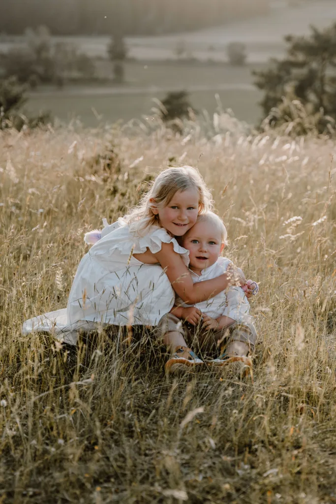 Geschwister umarmen sich lachend bei einem natürlichen Familienshooting auf einer Sommerwiese bei Rottweil