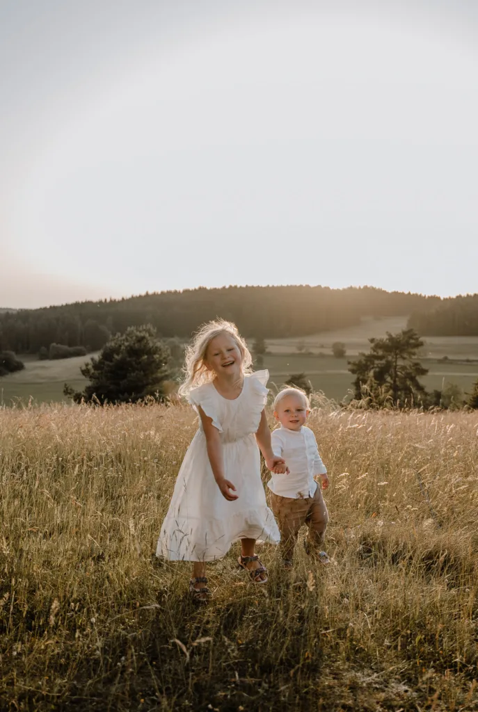 Zwei Kinder laufen Hand in Hand über eine Wiese bei einem Familienshooting in der Abendsonne bei Rottweil