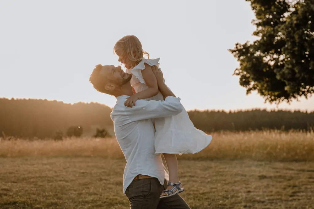 Papa hebt seine Tochter lachend bei einem natürlichen Familienshooting in der Abendsonne bei Rottweil hoch