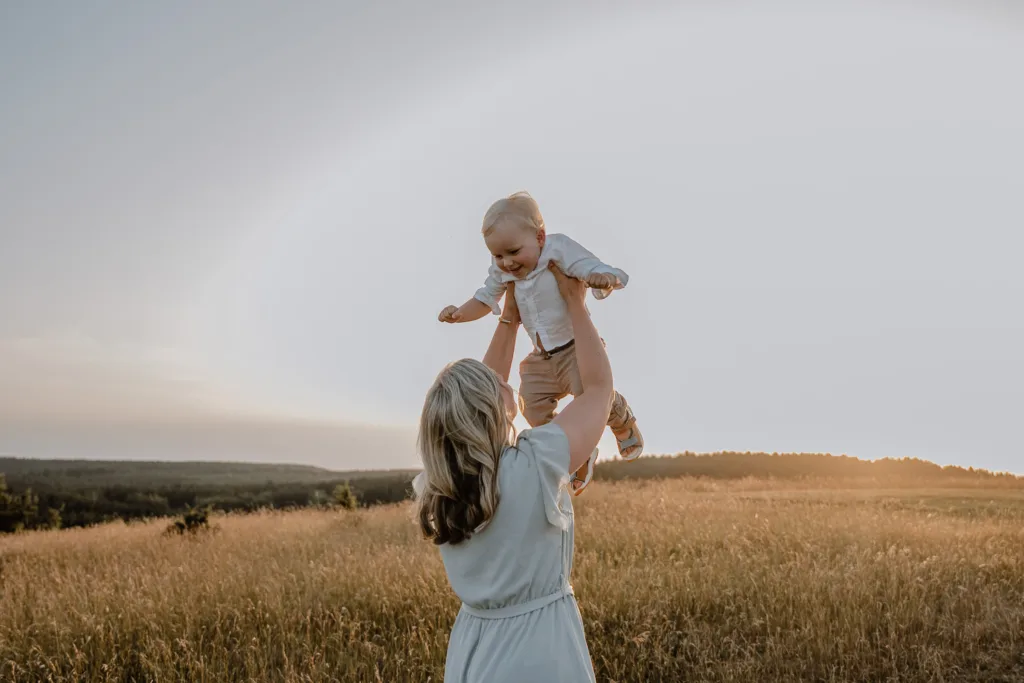 Mama hebt ihr Baby lachend bei einem natürlichen Familienshooting im Abendlicht bei Rottweil hoch