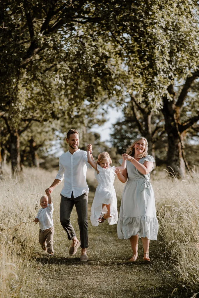 Fröhliche Familie mit zwei Kindern läuft Hand in Hand über einen Wiesenweg im warmen Abendlicht