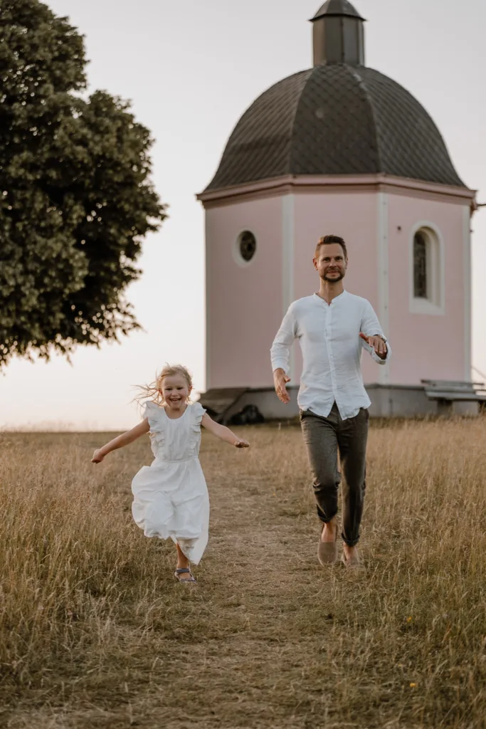 Vater und Tochter rennen lachend bei einem natürlichen Familienshooting vor einer Kapelle bei Rottweil