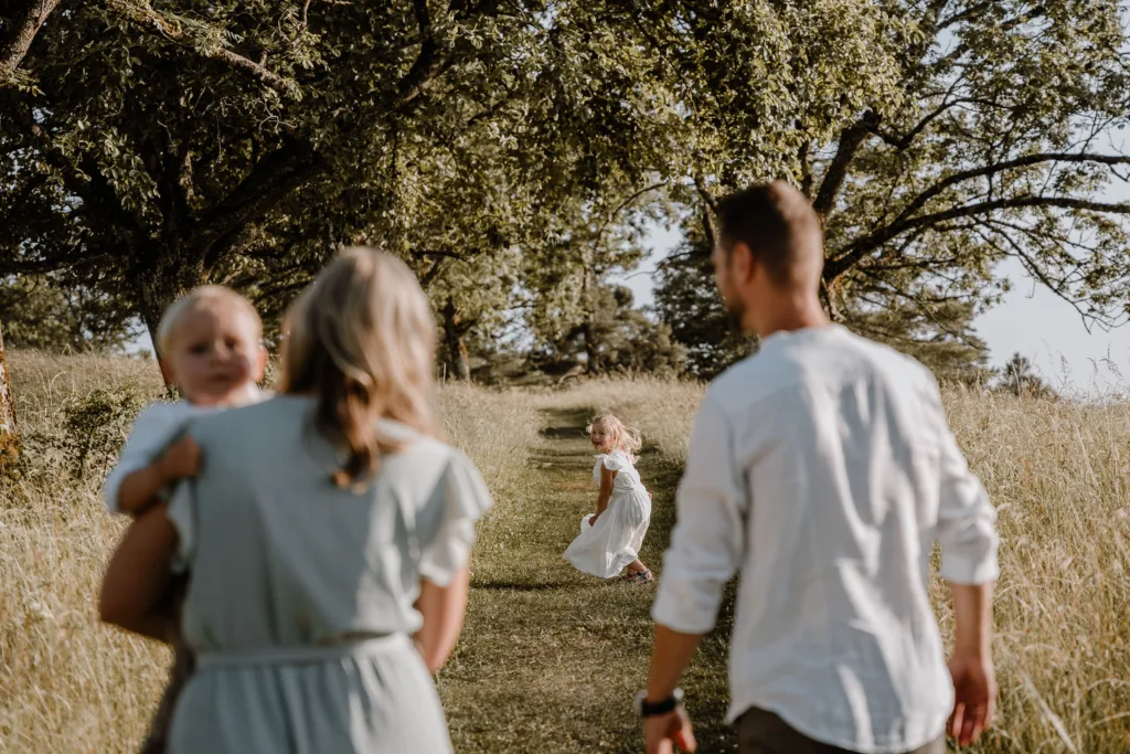 Kleines Mädchen dreht sich lachend um, während ihre Familie ihr auf dem Wiesenweg folgt