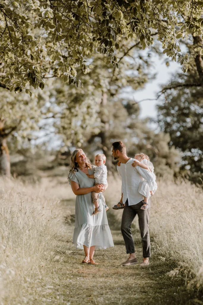 Familie steht zusammen auf einem Wiesenweg, Eltern tragen ihre Kinder auf dem Arm