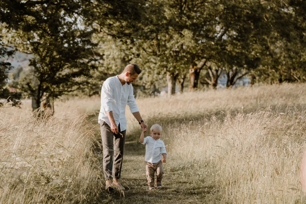 Vater geht Hand in Hand mit seinem kleinen Sohn über einen Wiesenweg
