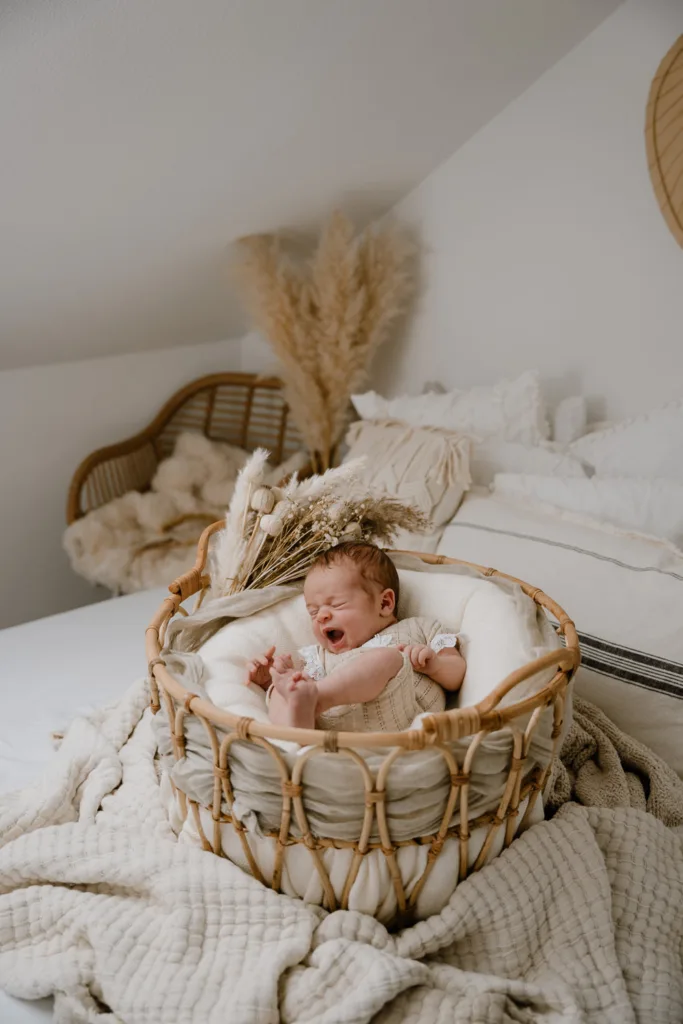 Neugeborenenshooting- gähnendes Baby liegt in Korb und wird fotografiert
