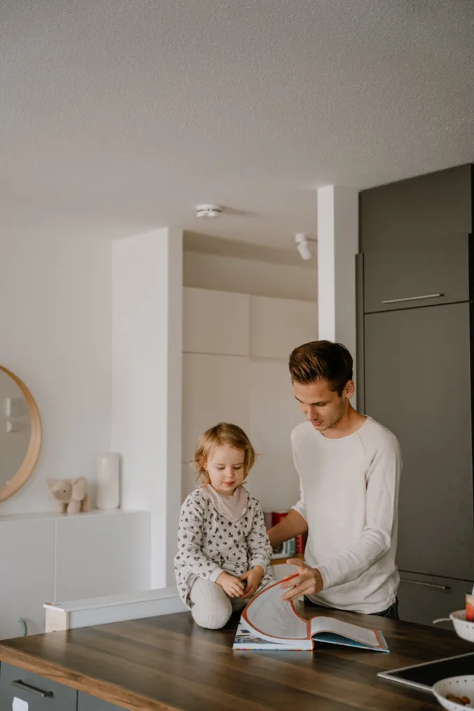 Vater ist mit seiner Tochter in der Küche und liest ihr ein Buch vor.