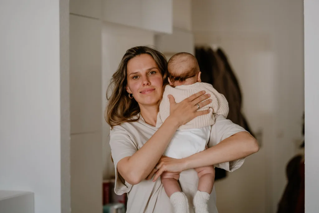 Mutter schaut in Kamera und klopft mit der Hand ihrem kleinen Baby auf den Rücken.