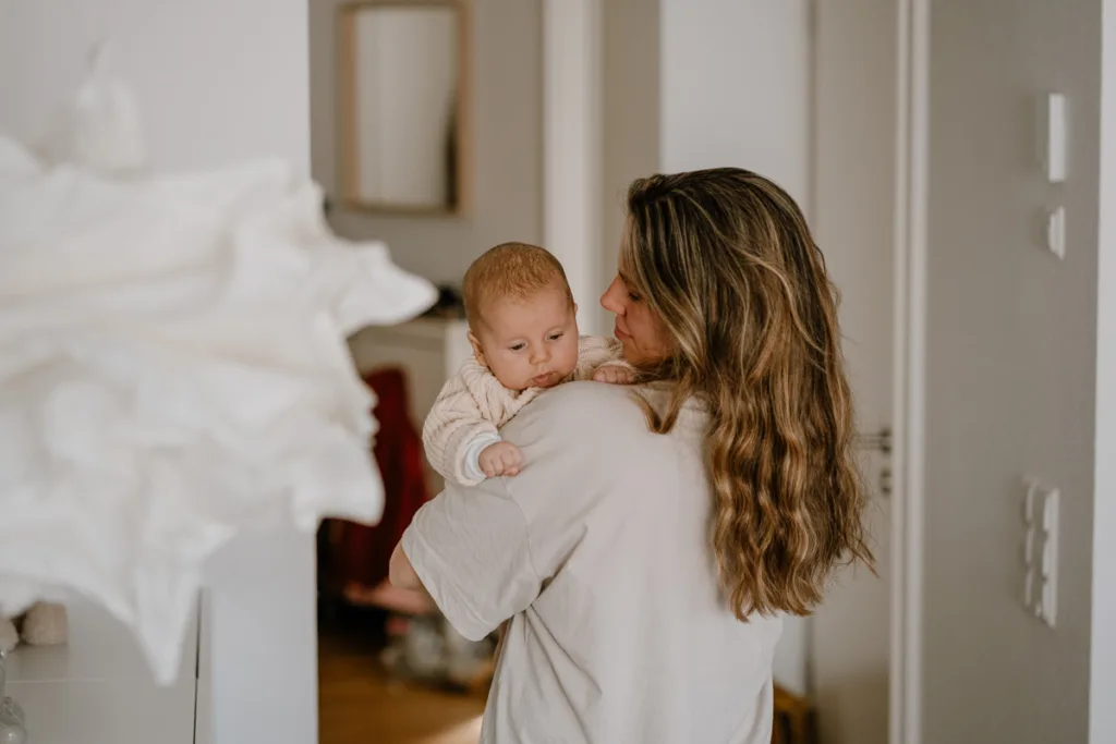 Mutter steht im Flur und hat ihr Baby auf dem Arm. Das Baby schaut aufgeregt über die Schulter.