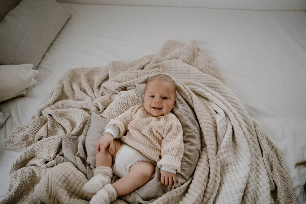 Ein Baby liegt lachend und entspannt auf weichen Decken und schaut aufmerksam in die Kamera