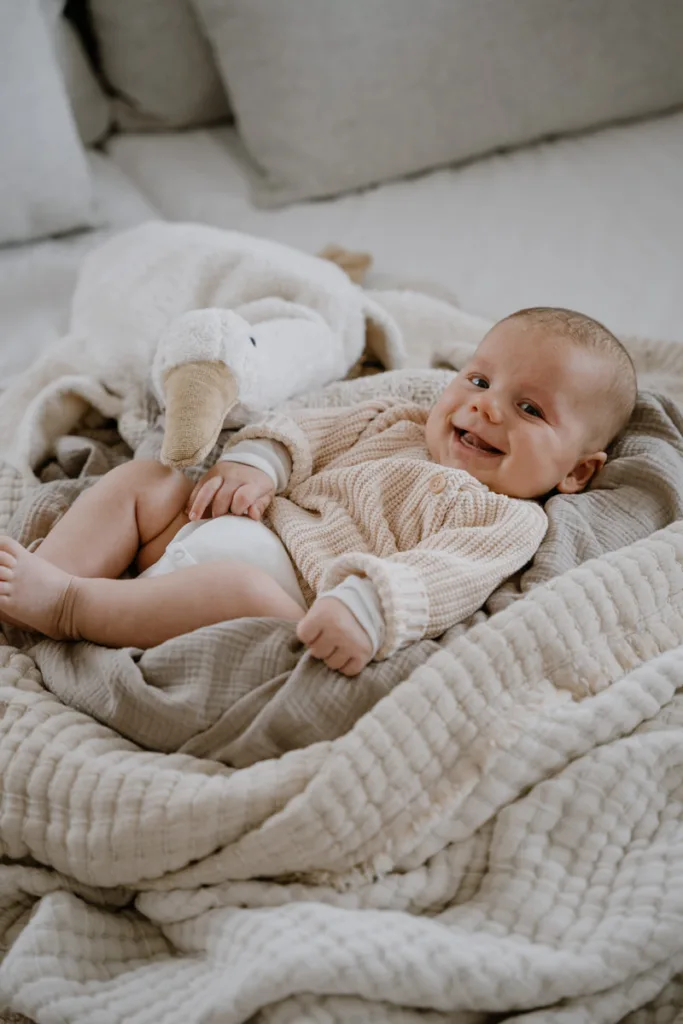 Ein Baby liegt lachend und entspannt auf weichen Decken und schaut aufmerksam in die Kamera