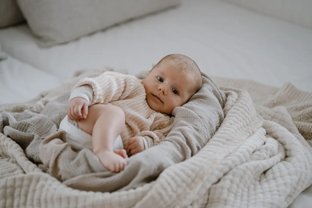 Ein Baby liegt entspannt auf weichen Decken und schaut aufmerksam in die Kamera