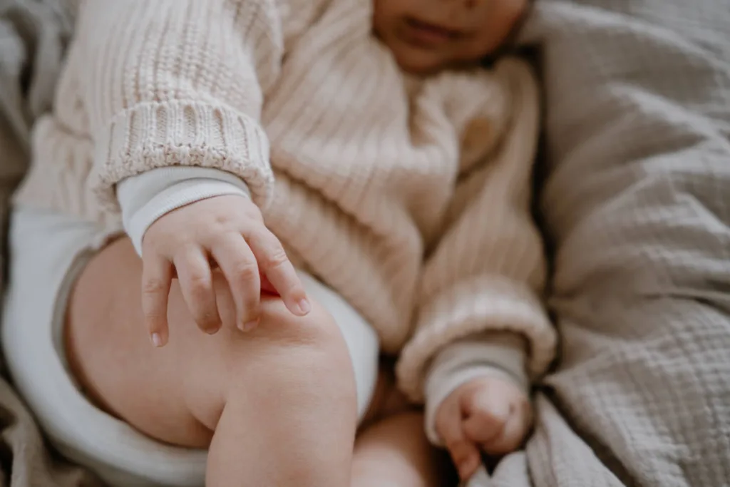 Bildausschnitt eines Babys, welches sich mit seiner kleinen Babyhand am Oberschenkel berührt.