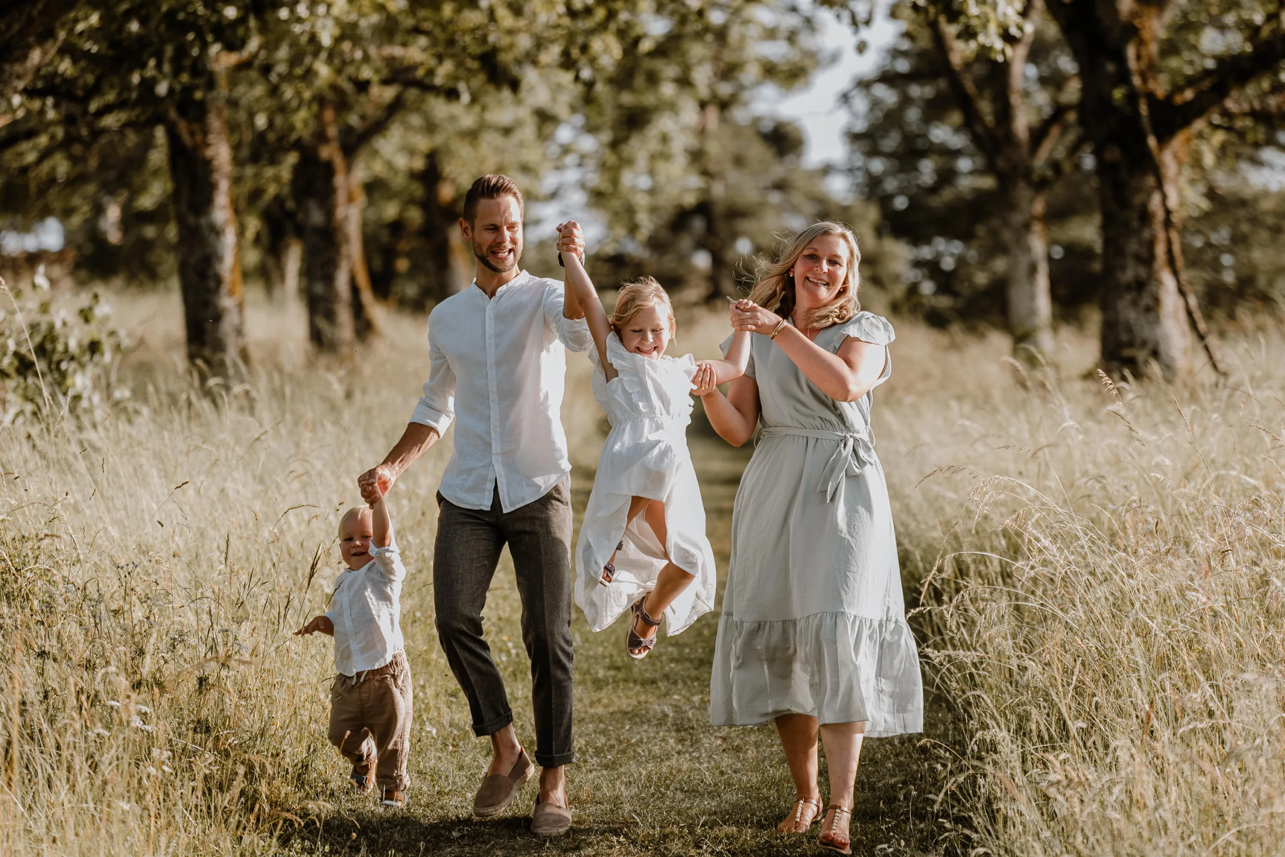Familie mit zwei Kindern läuft lachend über einen Wiesenweg bei einem Familienshooting im Freien