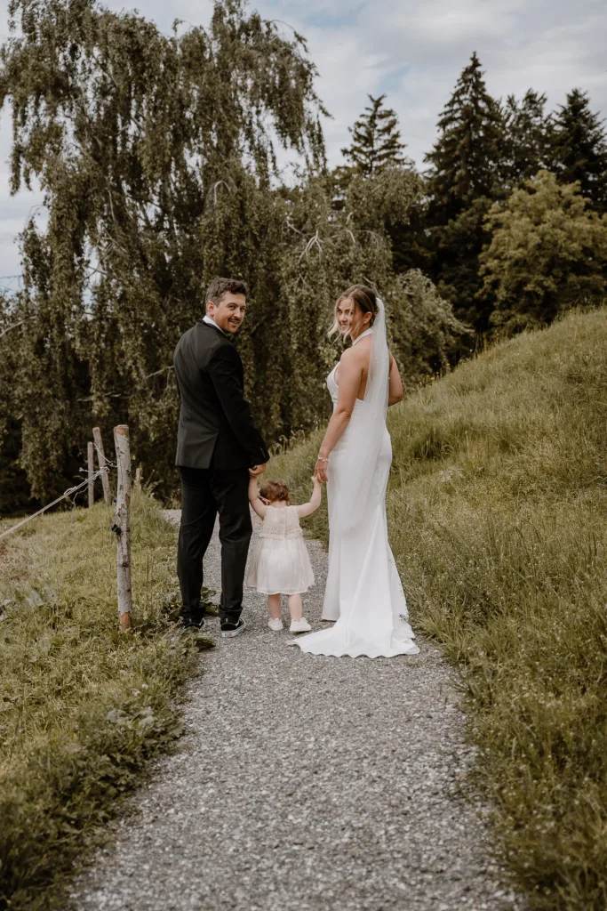 Brautpaar mit Kind läuft Hand in Hand einen Weg entlang bei einer Hochzeit in Österreich, natürliche Hochzeitsfotografie in den Bergen.