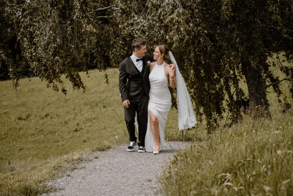 Braut und Bräutigam spazieren Arm in Arm durch die Natur bei einer Hochzeit in Österreich.
