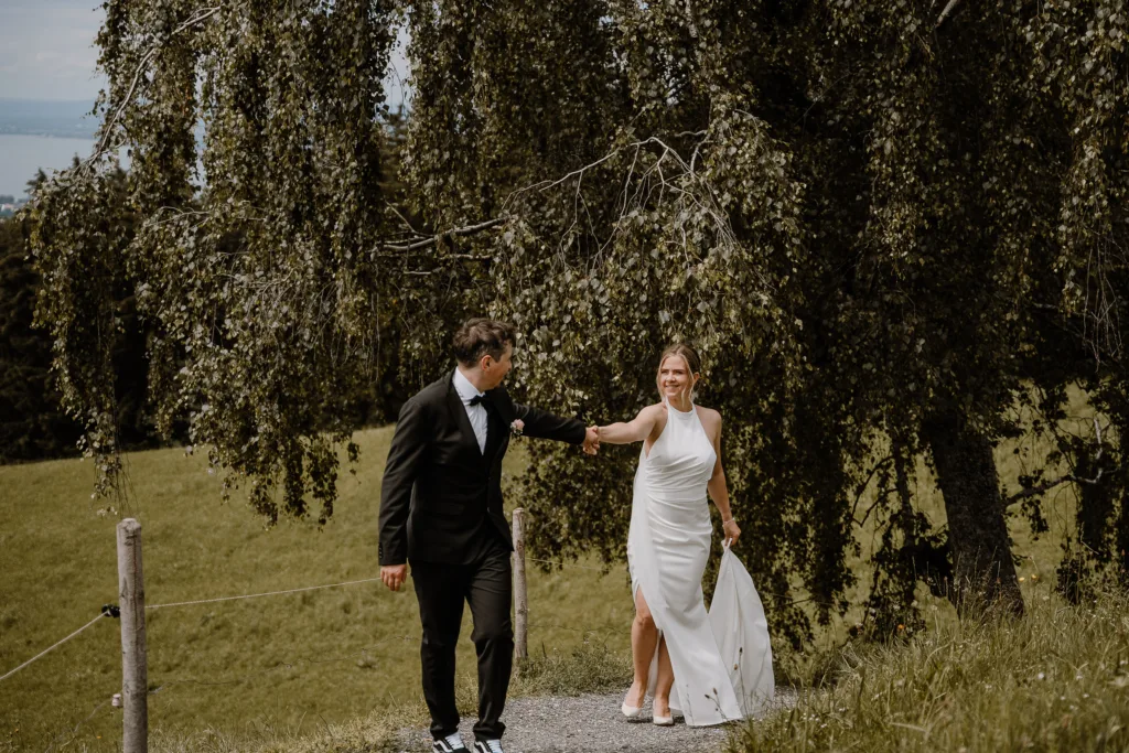 Brautpaar hält sich an den Händen bei einer Hochzeit in der Natur Österreichs, umgeben von Bäumen.
