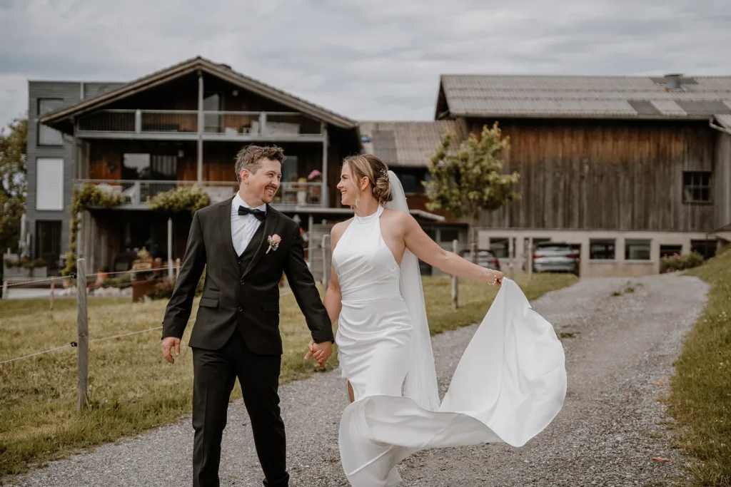 Brautpaar läuft Hand in Hand vor einer ländlichen Hochzeitslocation in Österreich.