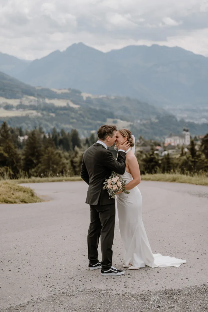Brautpaar küsst sich liebevoll bei einer Hochzeit in den Bergen Österreichs mit weiter Aussicht.