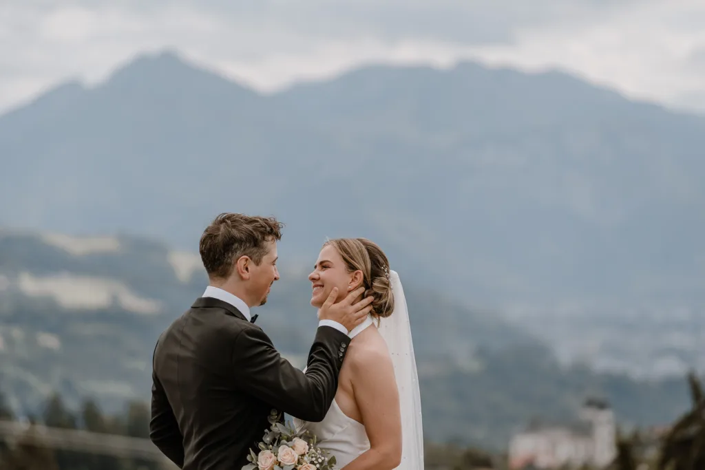 Bräutigam berührt das Gesicht der Braut bei einer Hochzeit in Österreich, Berge im Hintergrund.