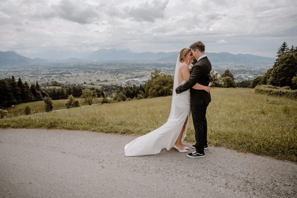 Braut und Bräutigam umarmen sich auf einer Wiese mit Blick über das Tal bei einer Hochzeit in Österreich.