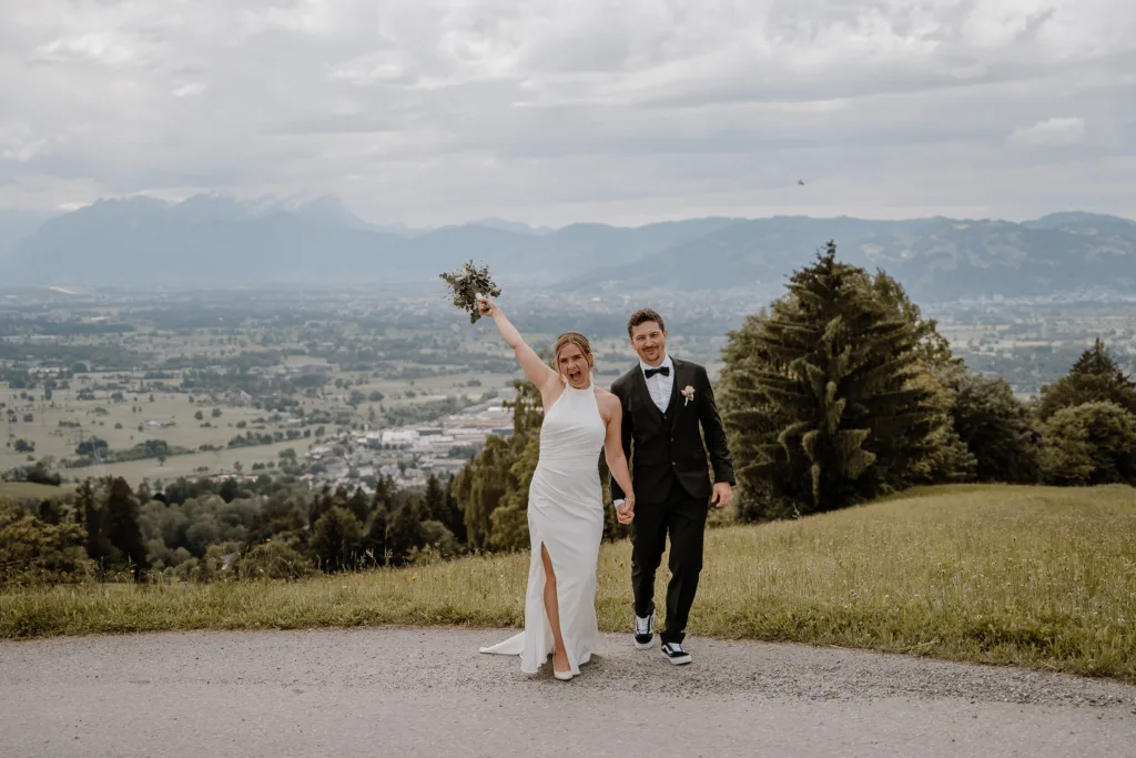 Brautpaar jubelt Hand in Hand bei einer Hochzeit in den Bergen Österreichs.