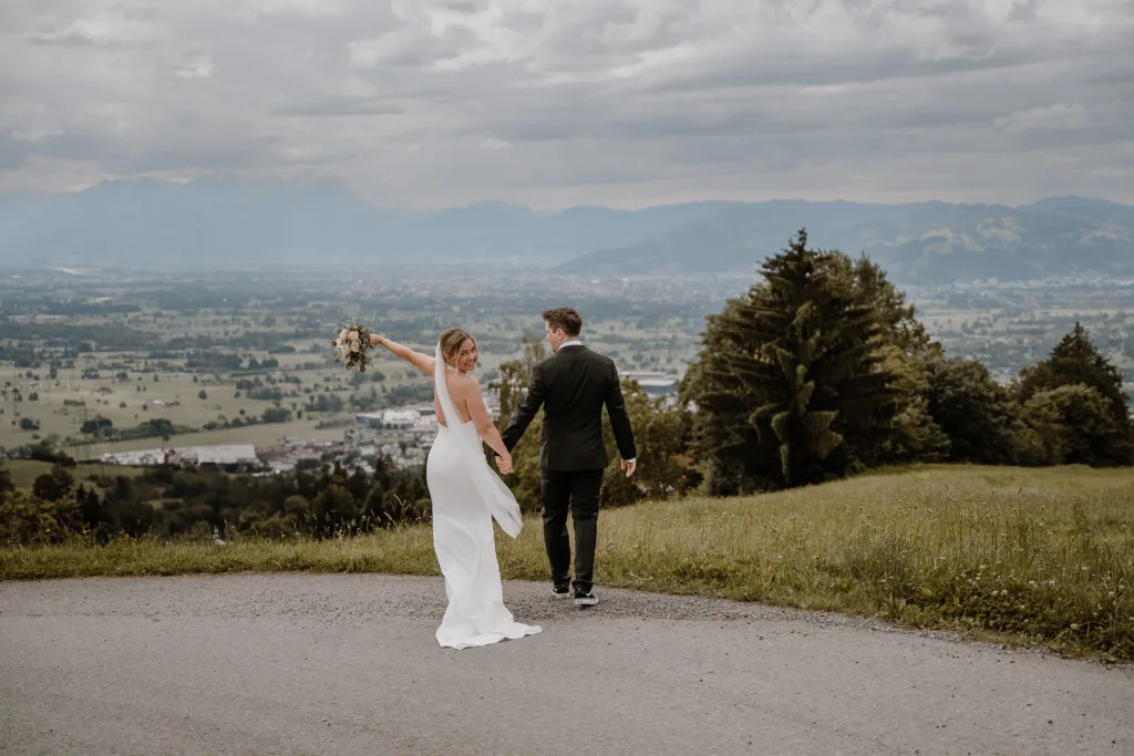Braut und Bräutigam gehen Hand in Hand mit Blick auf das Tal bei einer Hochzeit in Österreich.