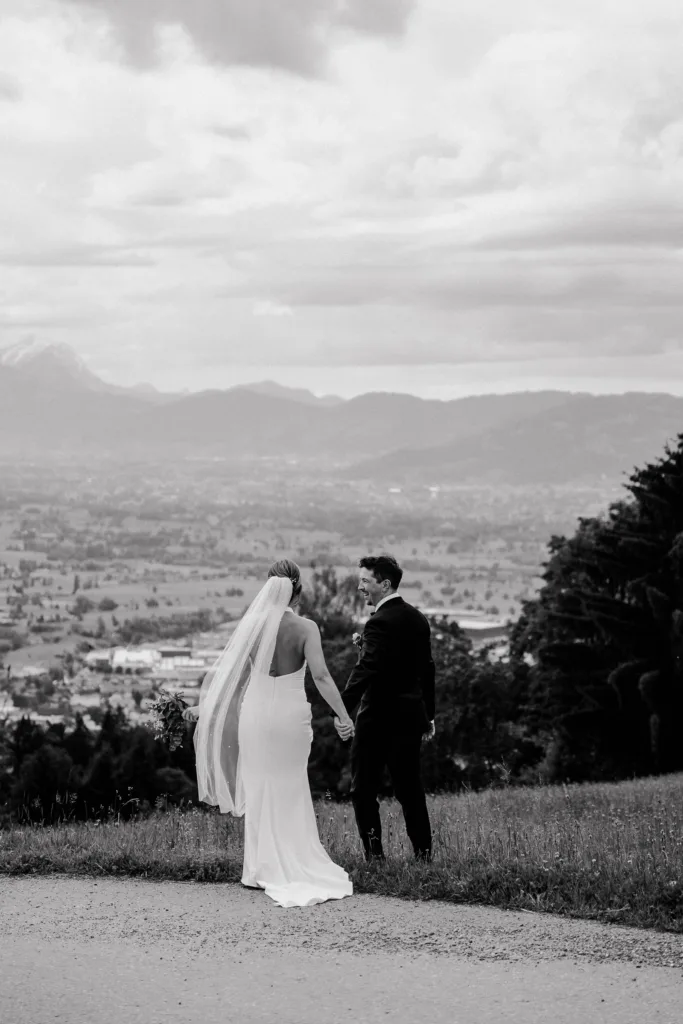 Schwarzweißes Hochzeitsfoto eines Brautpaares von hinten mit Blick über die Landschaft Österreichs.