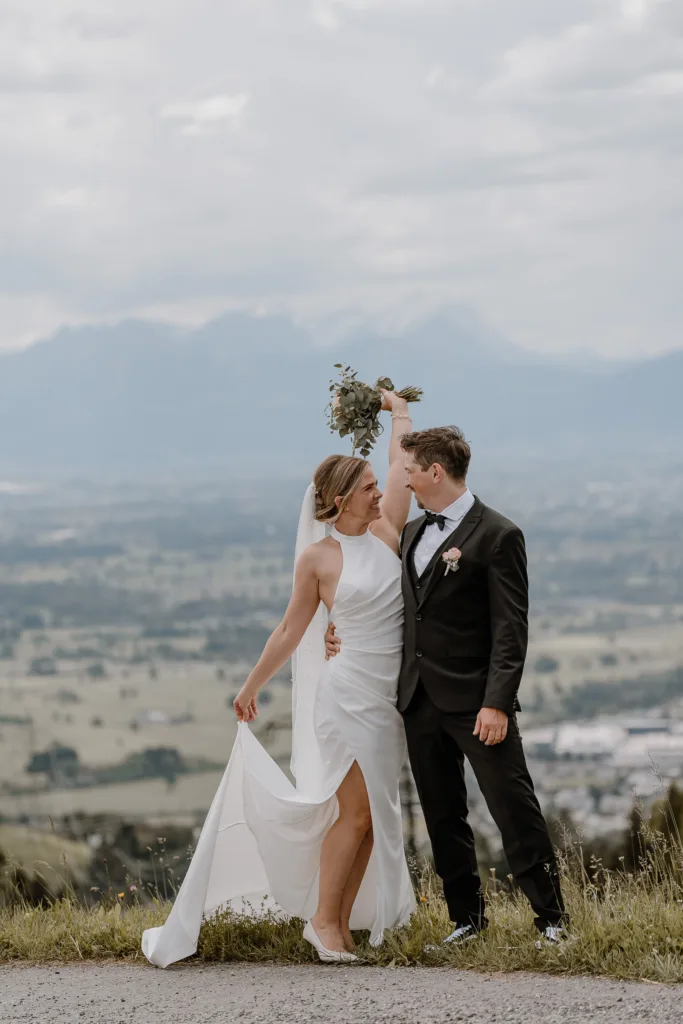 Braut hebt den Brautstrauß bei einer Hochzeit in den Bergen Österreichs, Bräutigam an ihrer Seite.