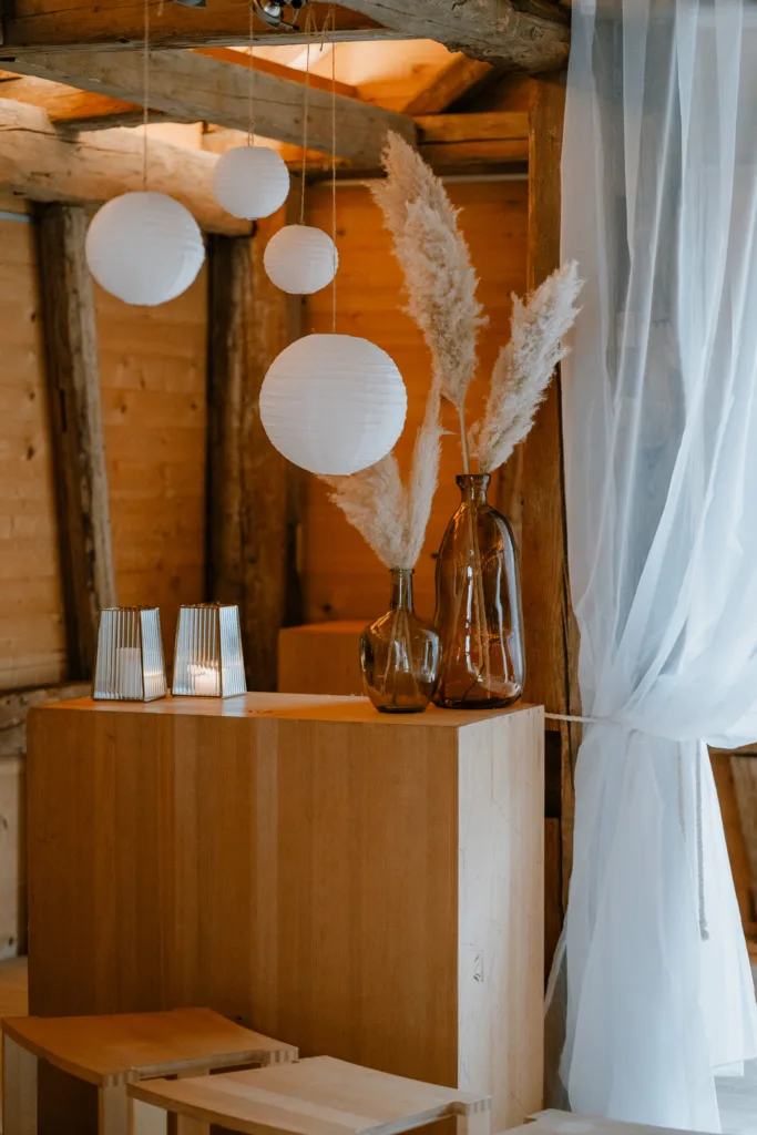 Detailaufnahme der Hochzeitsdekoration mit Glasvasen, Trockenblumen und Papierlampions in einer Scheune in Österreich.