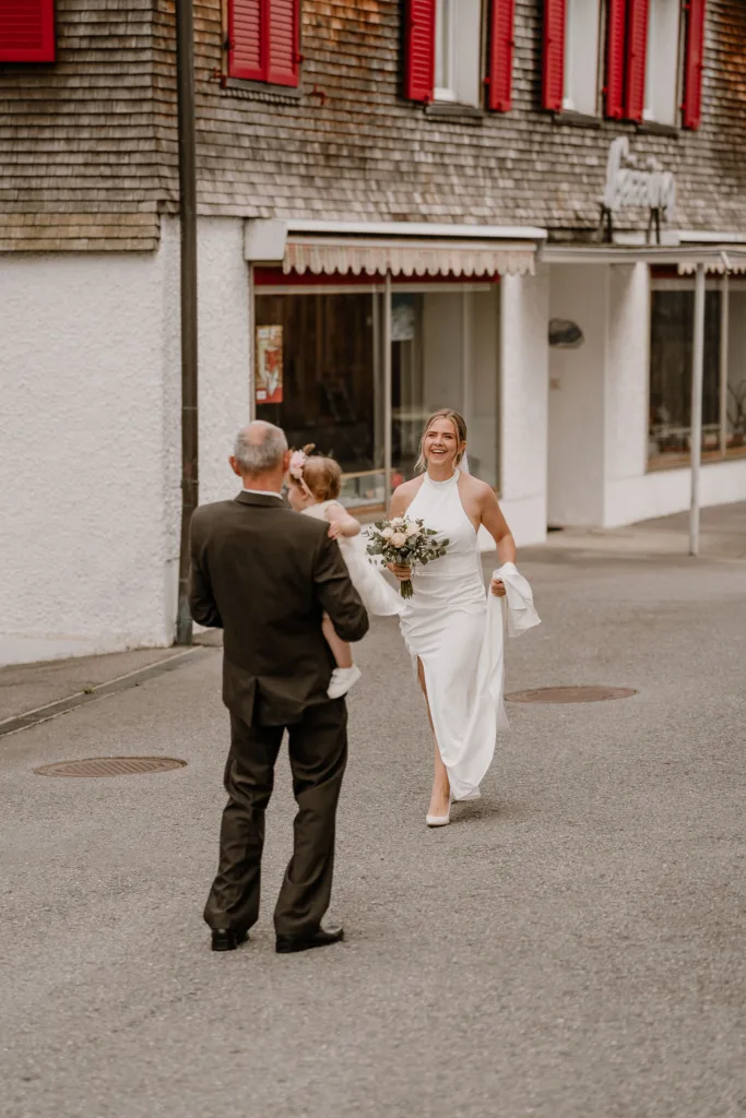 Braut läuft lächelnd mit Brautstrauß auf ihren Vater zu bei einer Hochzeit in Vorarlberg.