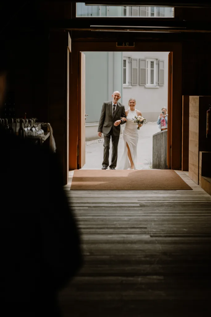 Braut wird von ihrem Vater durch den Eingang der Scheune zur Trauung geführt.