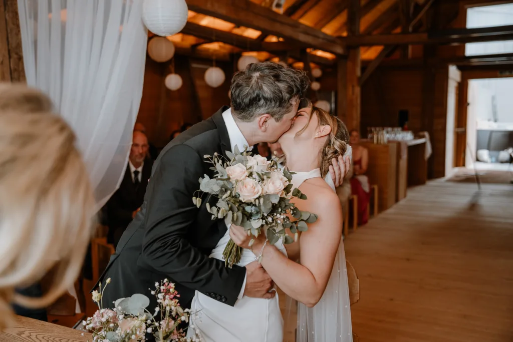 Braut und Bräutigam küssen sich nach der Trauung in einer rustikalen Scheune in Österreich.
