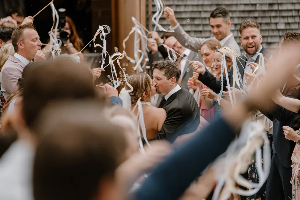 Brautpaar küsst sich im Spalier der Gäste, Seifenblasen fliegen durch die Luft.