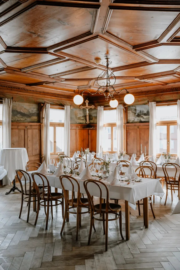 Festlich gedeckter Hochzeitsaal mit Holztischen, weißen Tischdecken und Holzstühlen.
