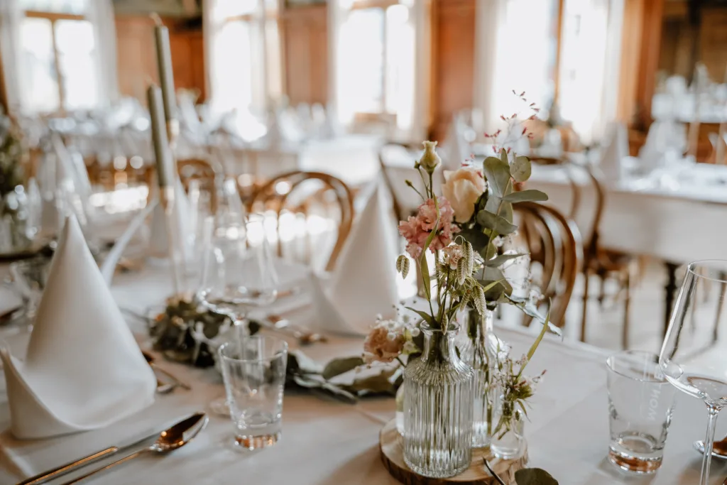 Detailaufnahme der Tischdekoration mit Glasvasen, Blumen und gefalteten Servietten.