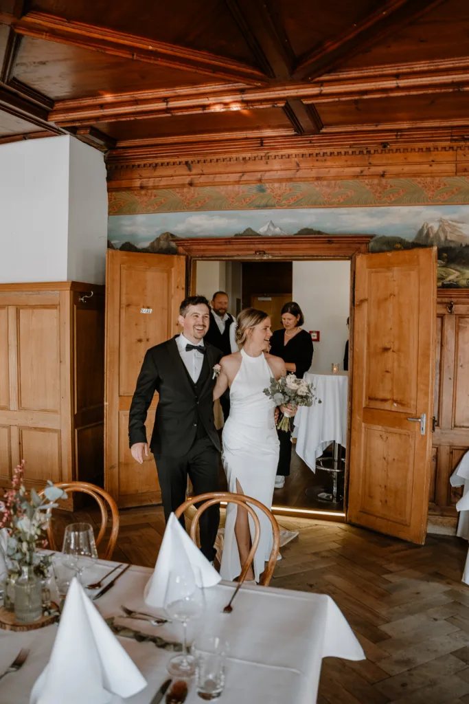 Braut und Bräutigam betreten den Hochzeitsaal durch eine Holztür.