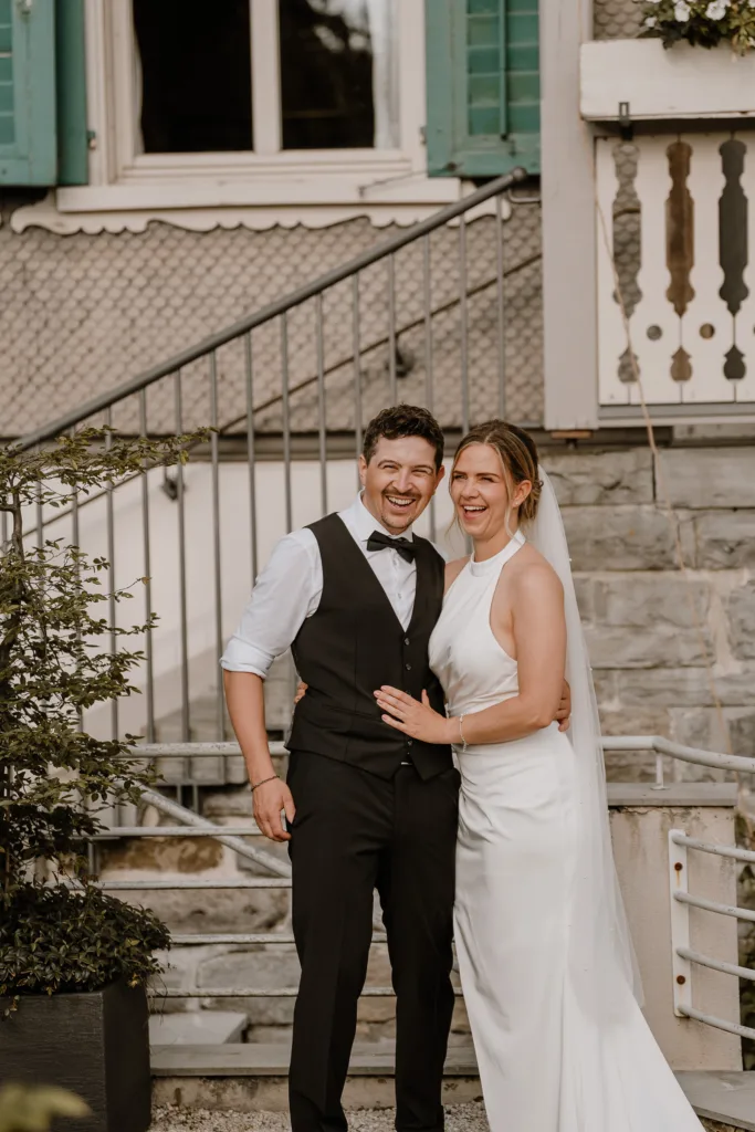 Braut und Bräutigam lachen in die Kamera vor dem Gasthaus.