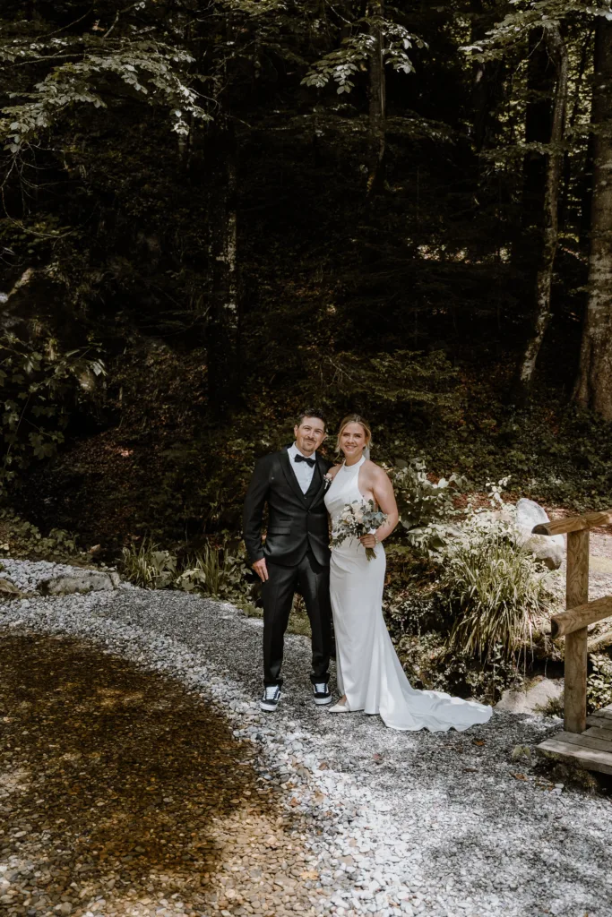 Brautpaar steht gemeinsam an einem Bach im Wald.