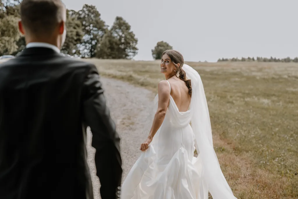 Braut blickt lächelnd über die Schulter auf Feldweg bei Rottweil