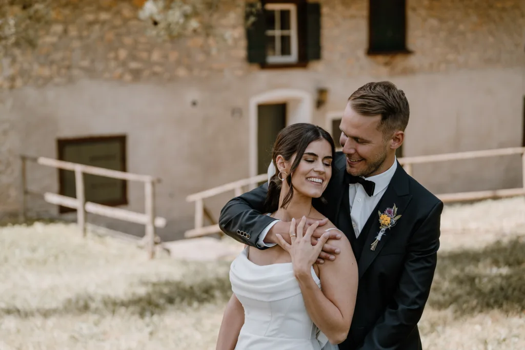 Brautpaar umarmt sich innig vor rustikalem Gebäude