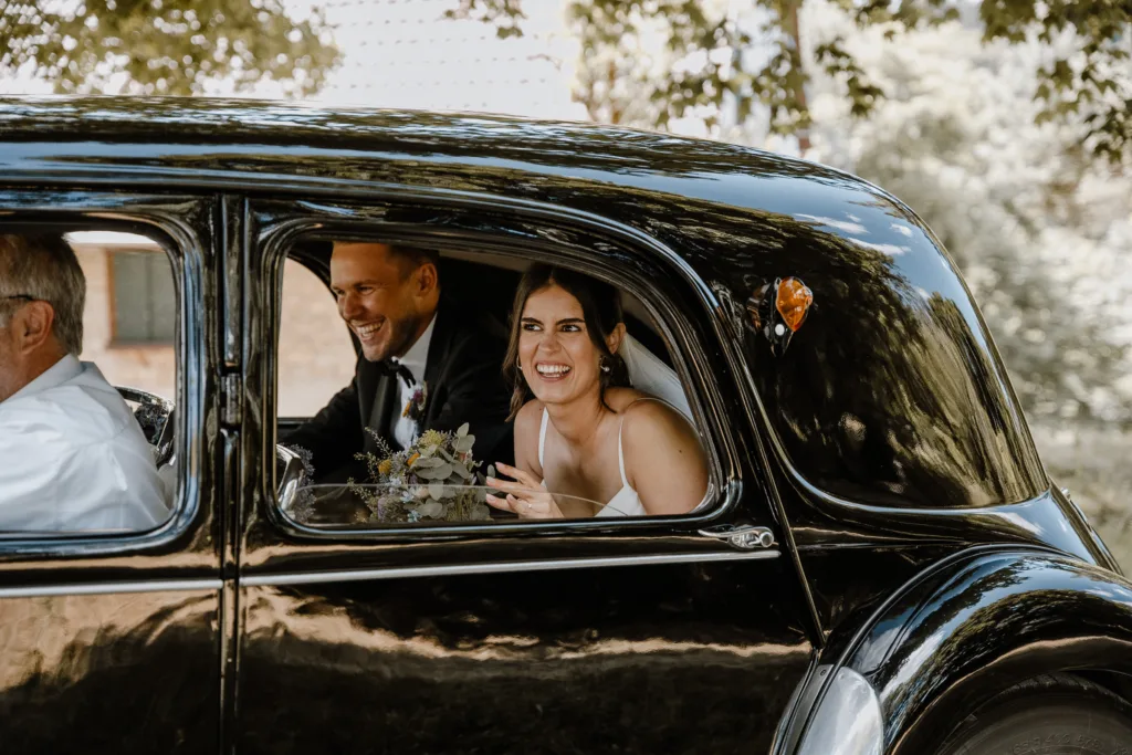 Glückliches Brautpaar im Oldtimer auf dem Weg zur Hochzeitsfeier