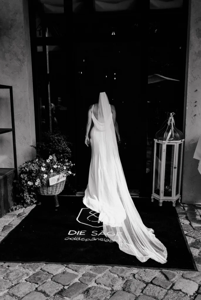 Braut betritt Hochzeitslocation von hinten mit langem Schleier