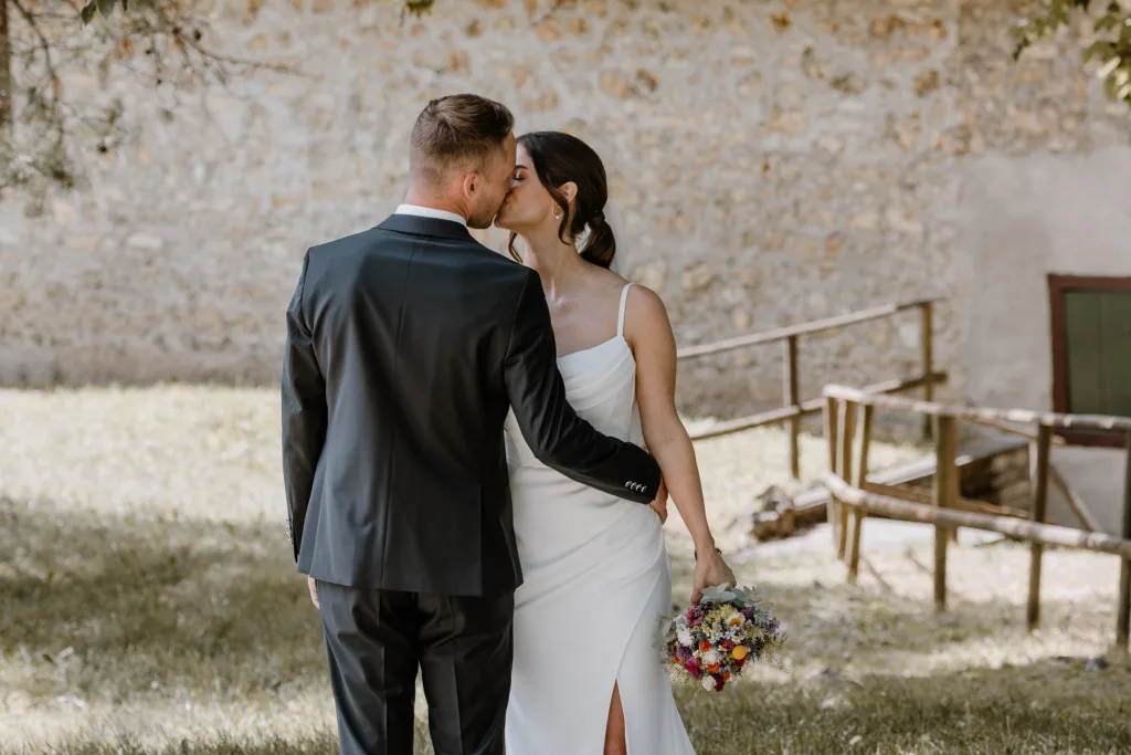 Brautpaar küsst sich vor historischer Steinmauer