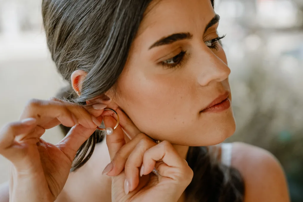 Braut steckt ihren Ohrring beim Getting Ready ein
